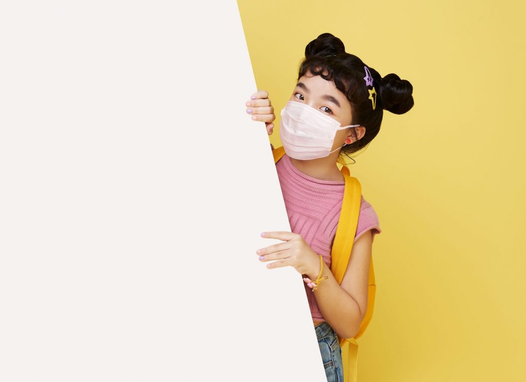 Smiling happy cute Asian child wearing mask to protect her from